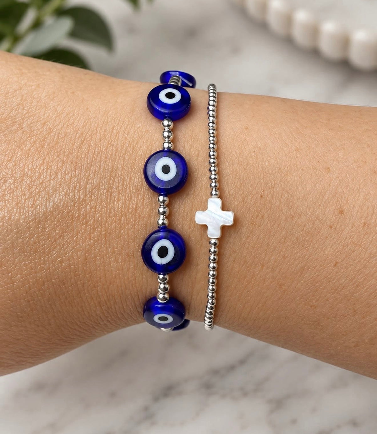 Blue evil eye bracelet shown beside a separate silver bead cross bracelet