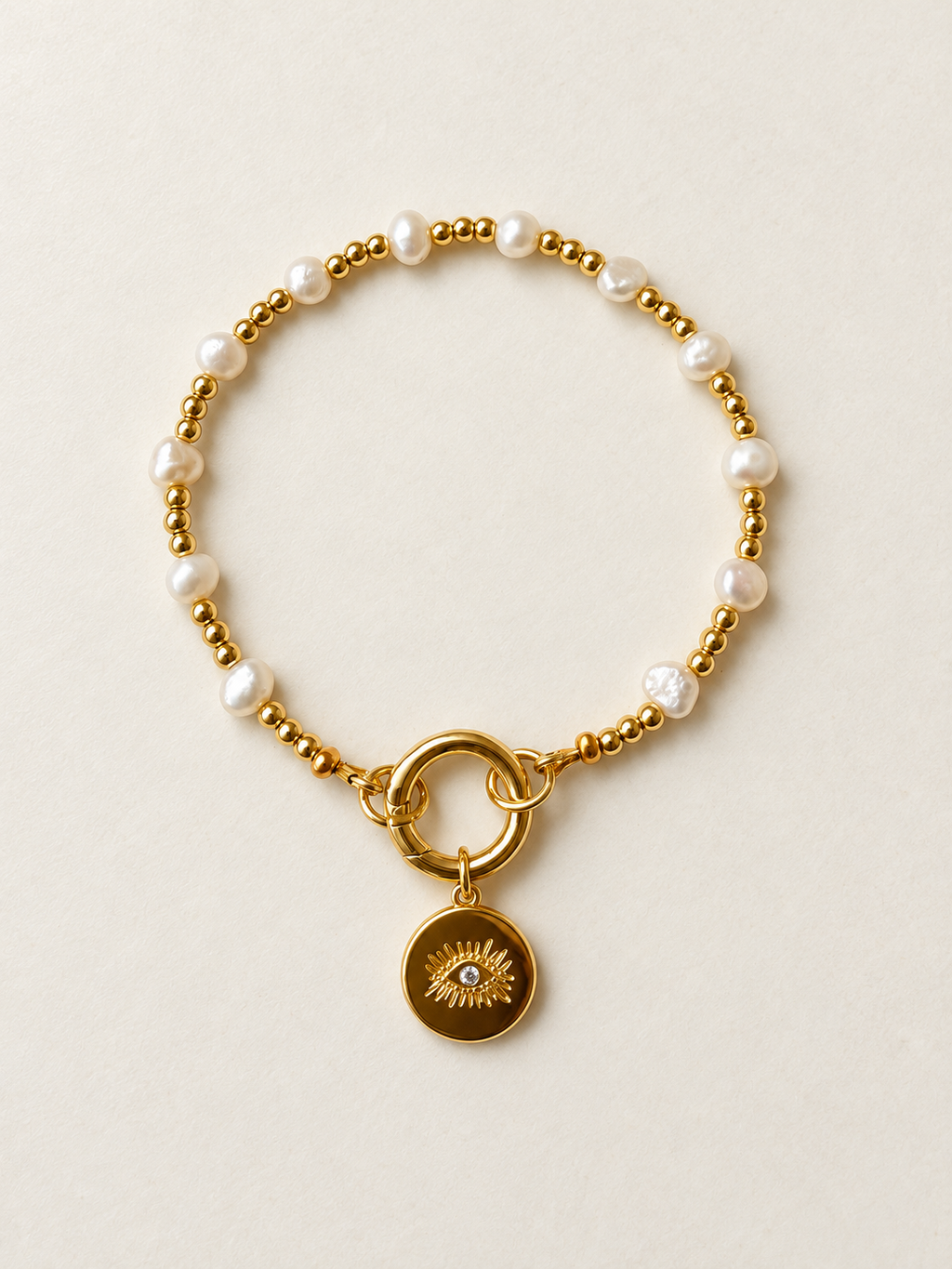 Pearl and gold charm bracelet with gold clasp and eye charm on an ivory background