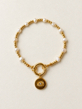 Pearl and gold charm bracelet with gold clasp and eye charm on an ivory background