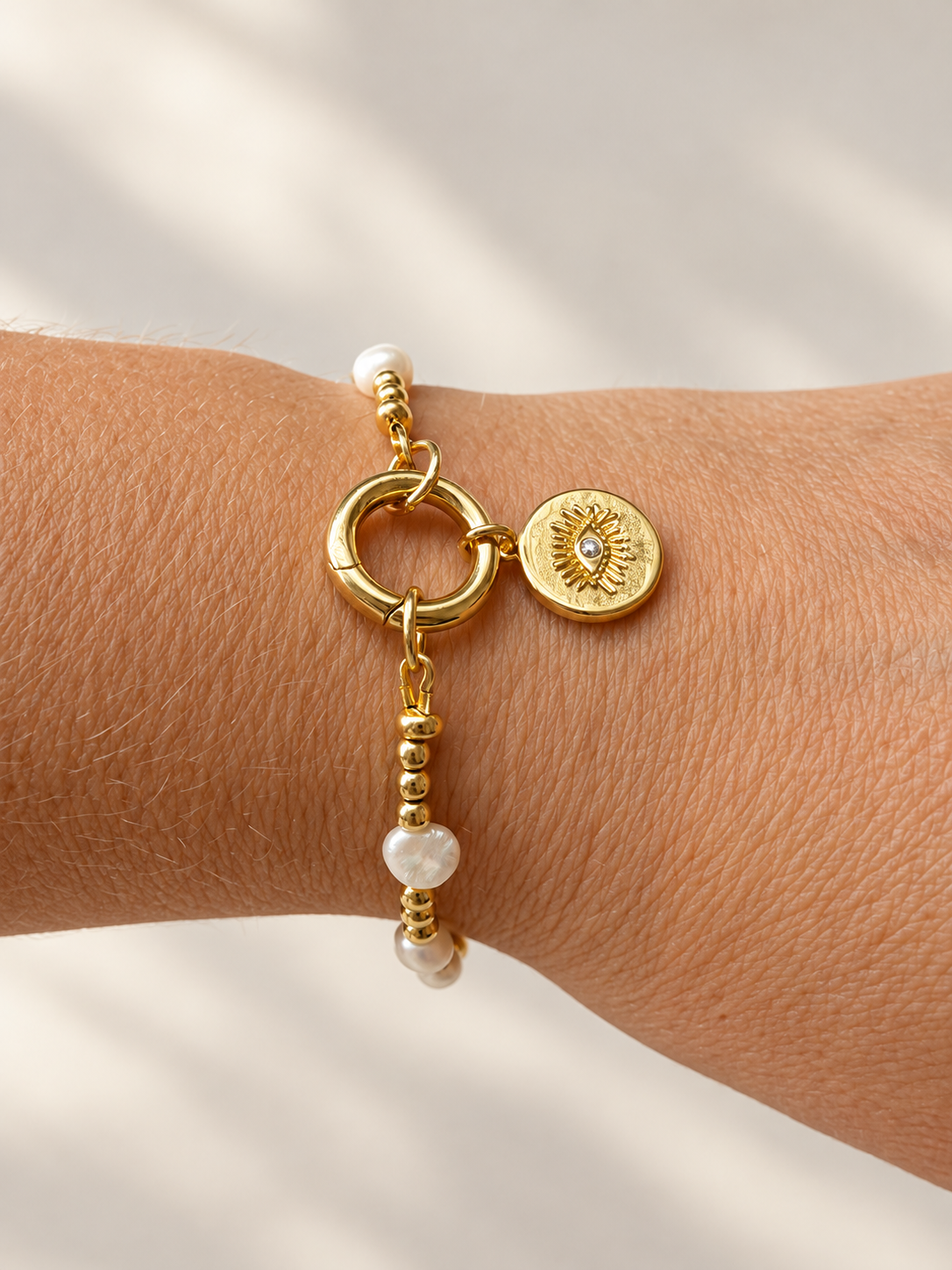 Pearl and gold charm bracelet shown on wrist with eye charm