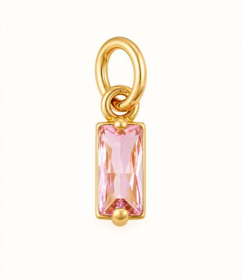 Single pink baguette crystal charm with gold-tone setting on off-white