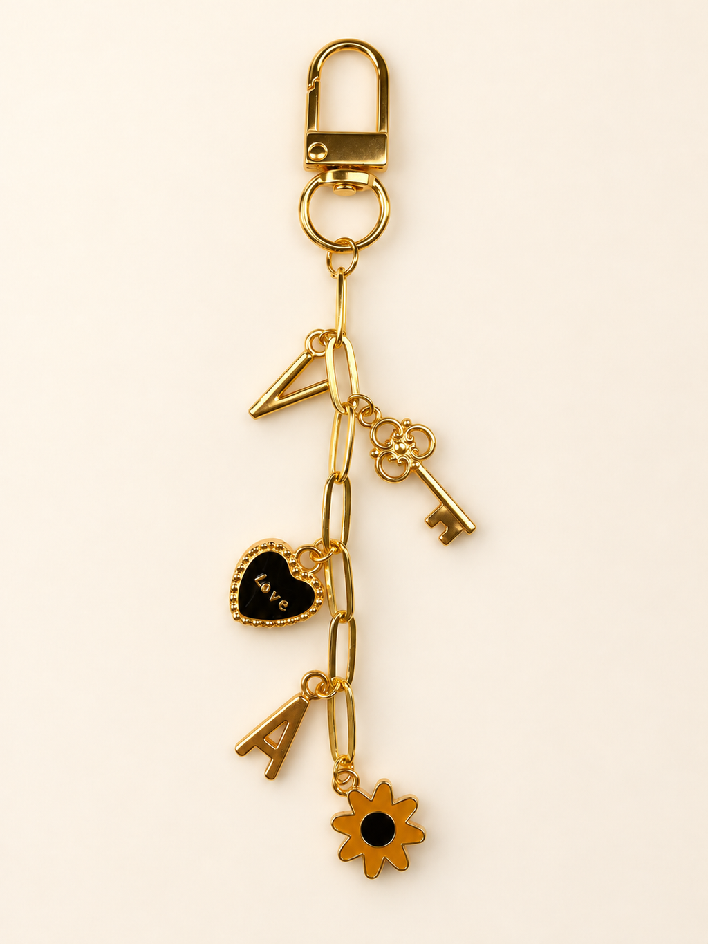 Gold-tone chain add-on for a bag charm with decorative charms shown on a warm ivory background