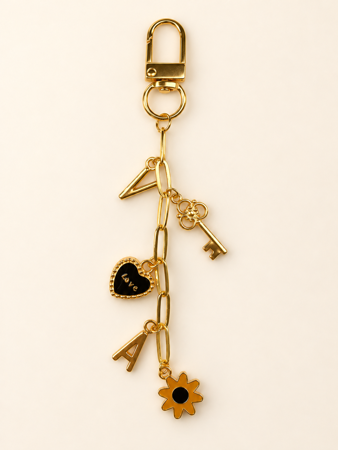 Gold-tone chain add-on for a bag charm with decorative charms shown on a warm ivory background
