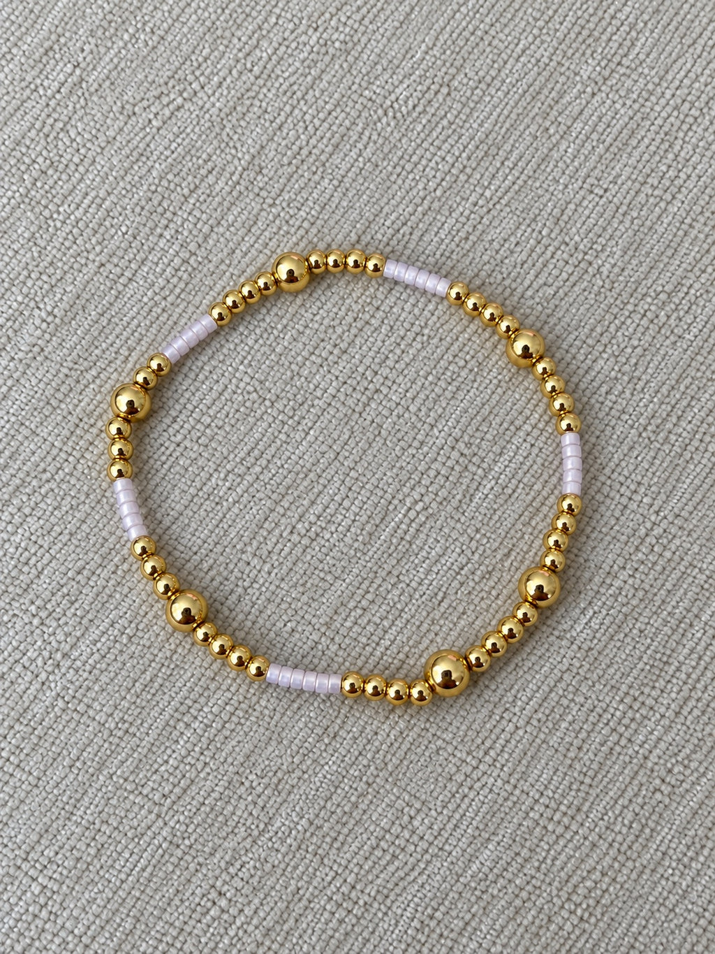 Lilac and gold beaded bracelet on neutral woven fabric