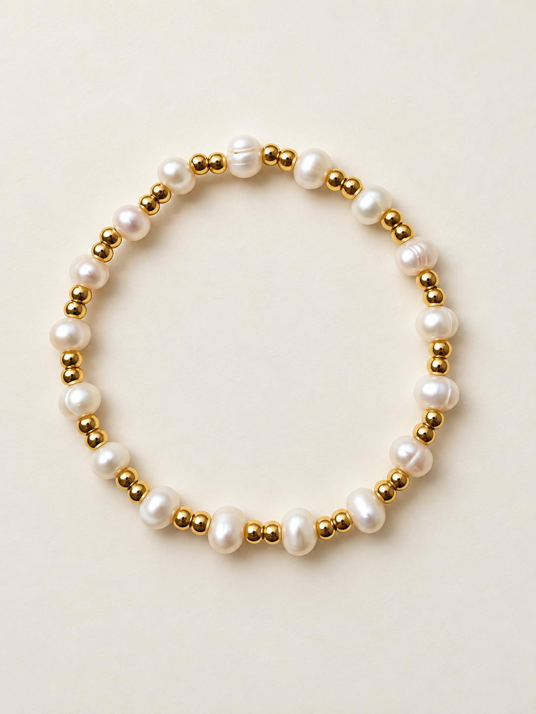 Ivory pearl bracelet with paired gold bead accents on an ivory background