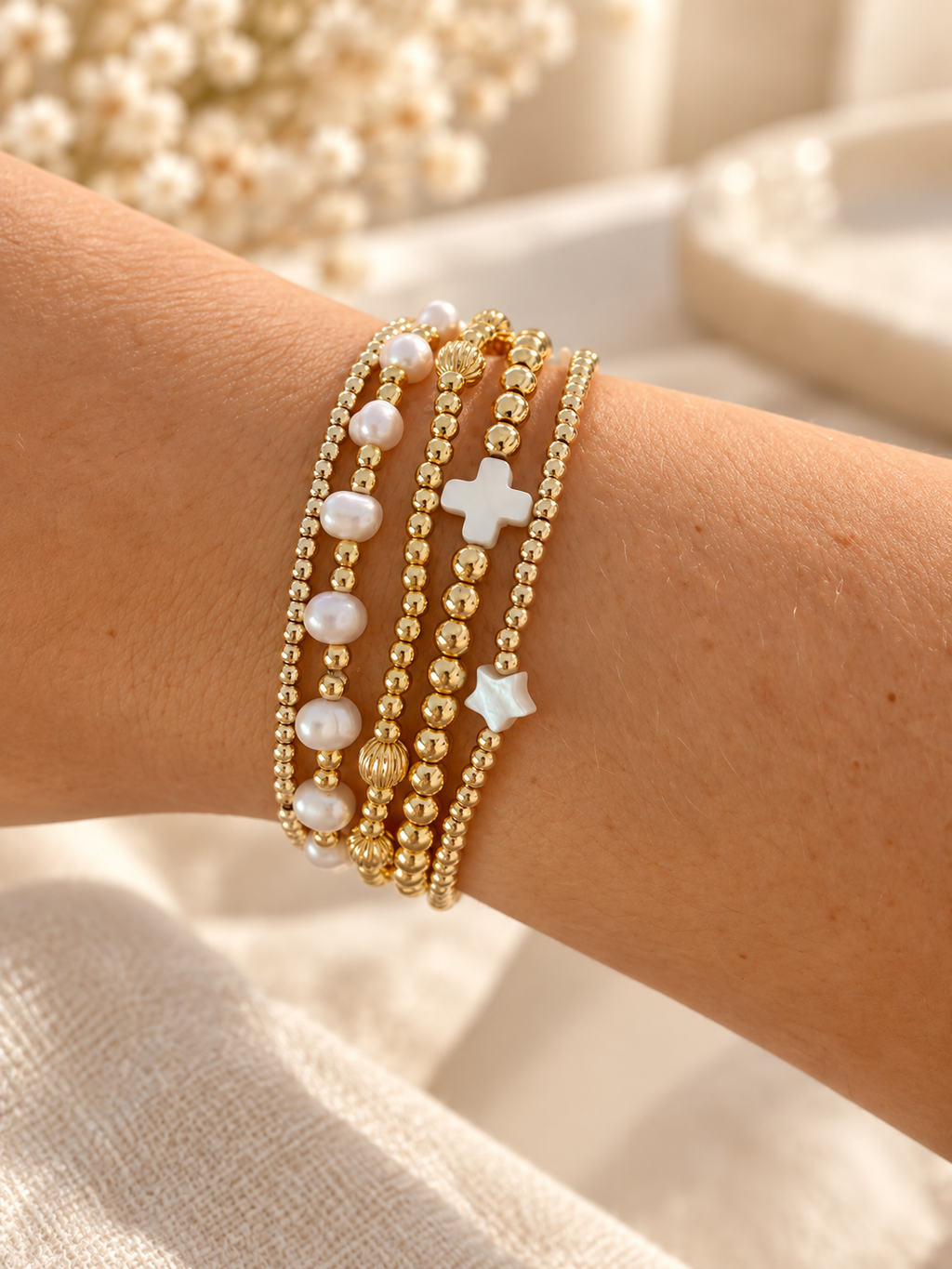 Pearl and gold bead bracelet stack with cross and star charms, styled on wrist