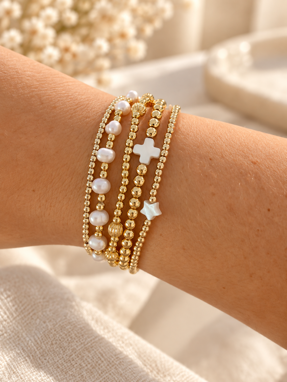 Pearl and gold bead bracelet stack with cross and star charms, styled on wrist