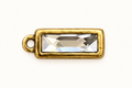Single clear rectangular crystal charm in gold-tone bezel on off-white