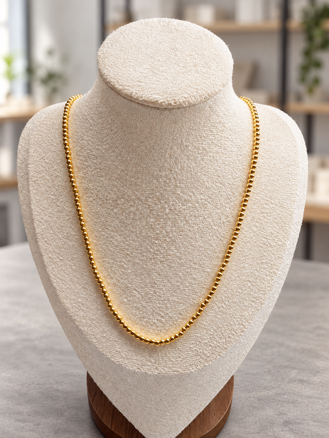 Simple gold beaded necklace on a display bust