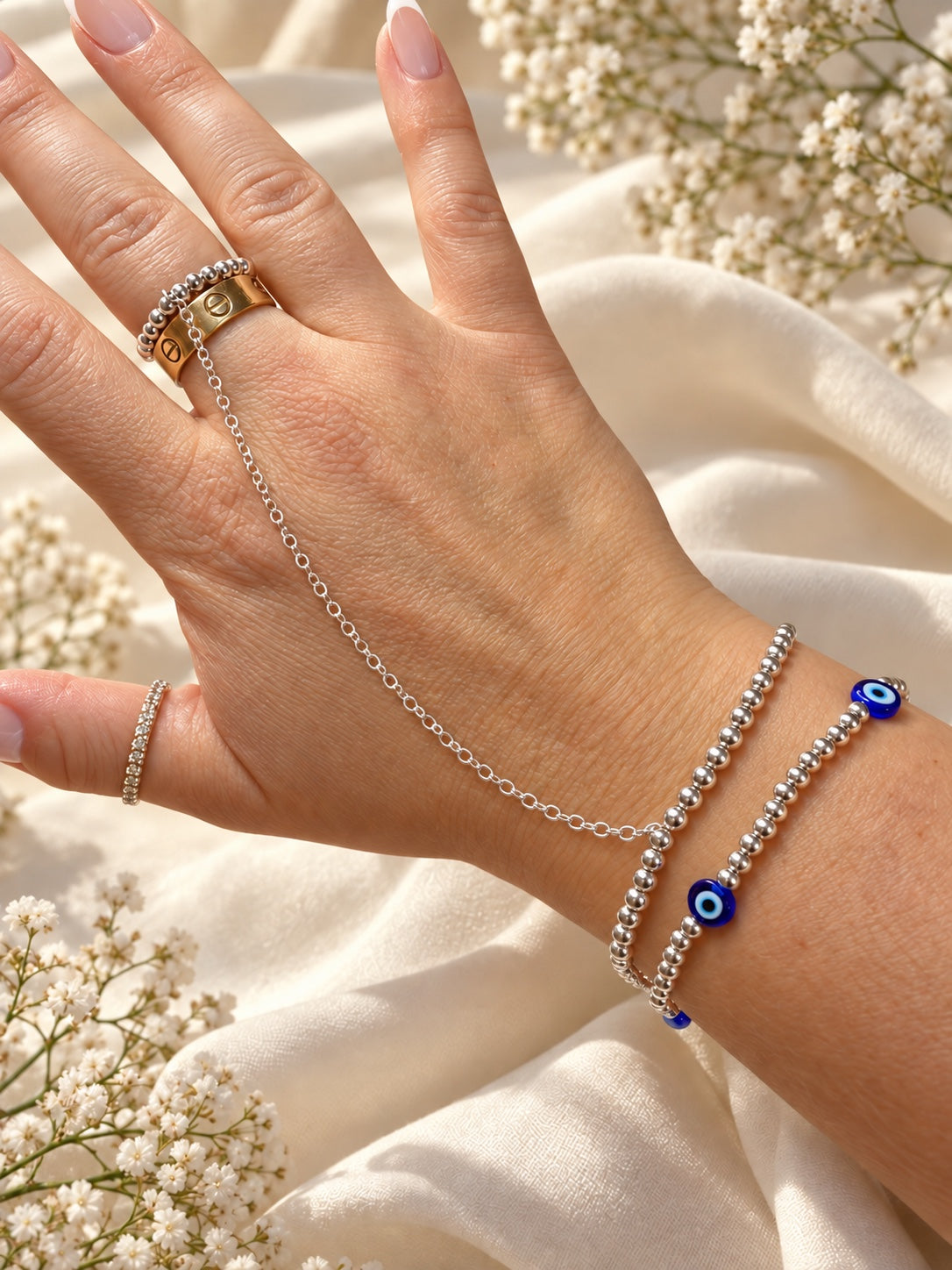 Small blue evil eye beads on a silver-tone bead bracelet styled with separate hand chain and rings