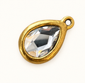 Single clear teardrop crystal charm in gold-tone bezel on off-white